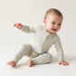 Happy baby in light green Bamboo Baby Romper, sitting with hand outstretched, laughing joyfully.